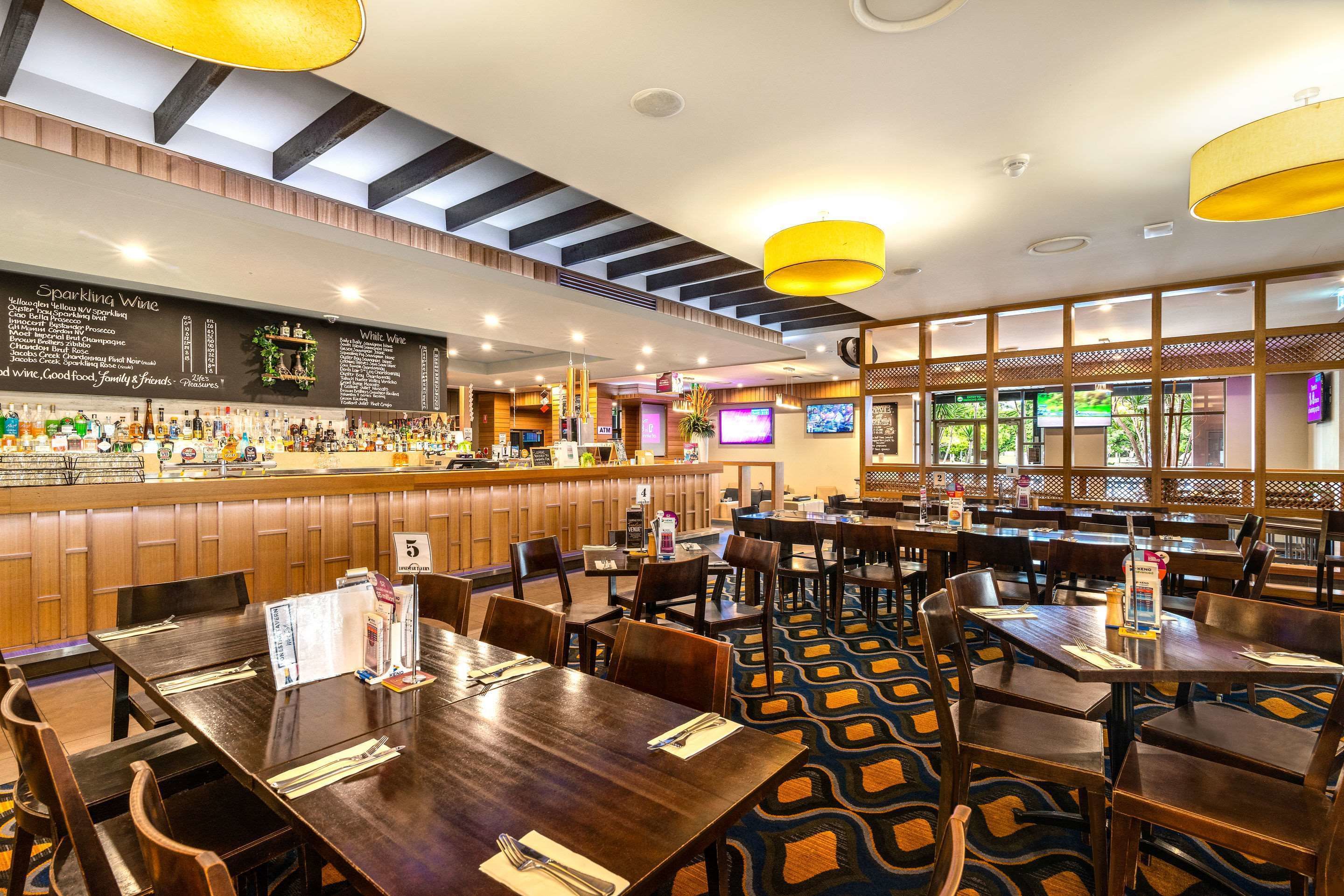 A restaurant with a bar area, wooden tables, and a patterned carpet.