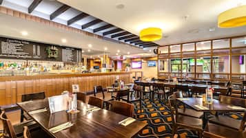 Um restaurante com área de bar, mesas de madeira e um tapete estampado.