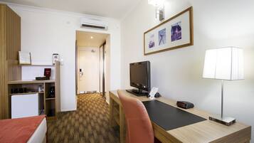 Ein Hotelzimmer mit Bett, Schreibtisch, Stuhl, Fernseher, Lampe und einem kleinen Kühlschrank.