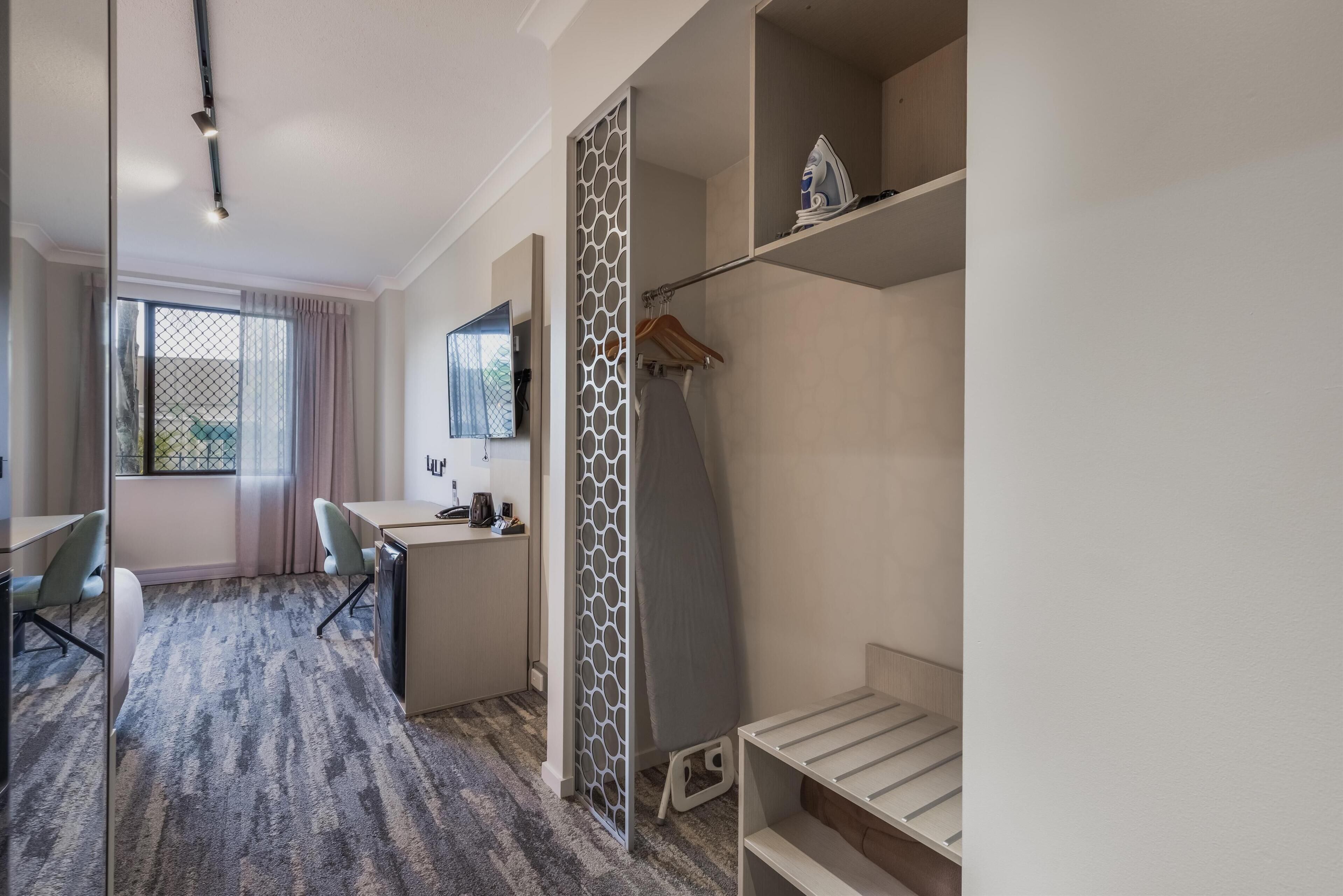 Une chambre d’hôtel de taille réduite, équipée d’un bureau, d’une chaise et d’un lit avec un espace de rangement intégré.
