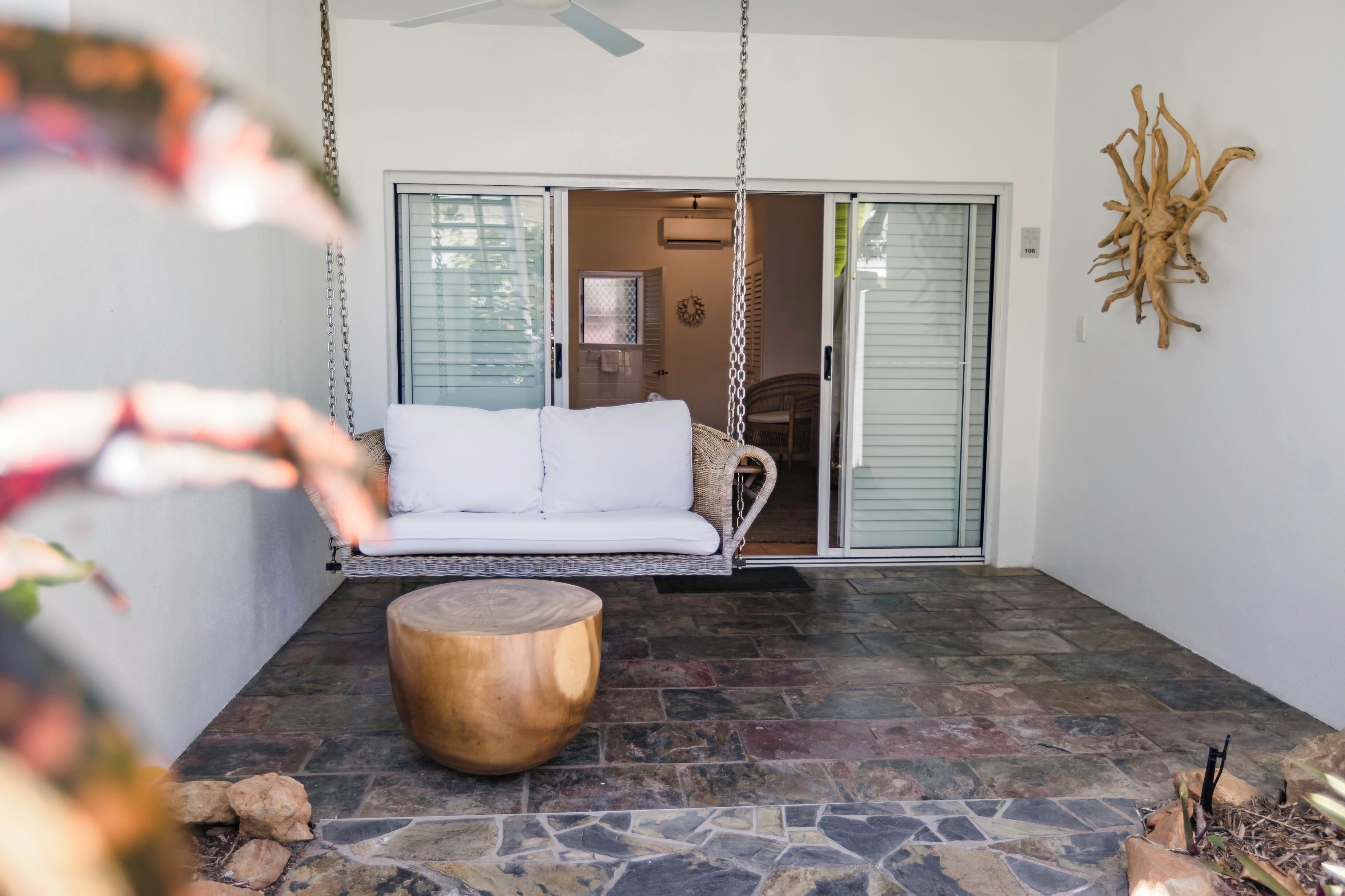 A patio with a white sofa, a wooden coffee table, and a hanging swing.