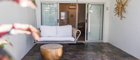 A patio with a white sofa, a wooden coffee table, and a hanging swing.