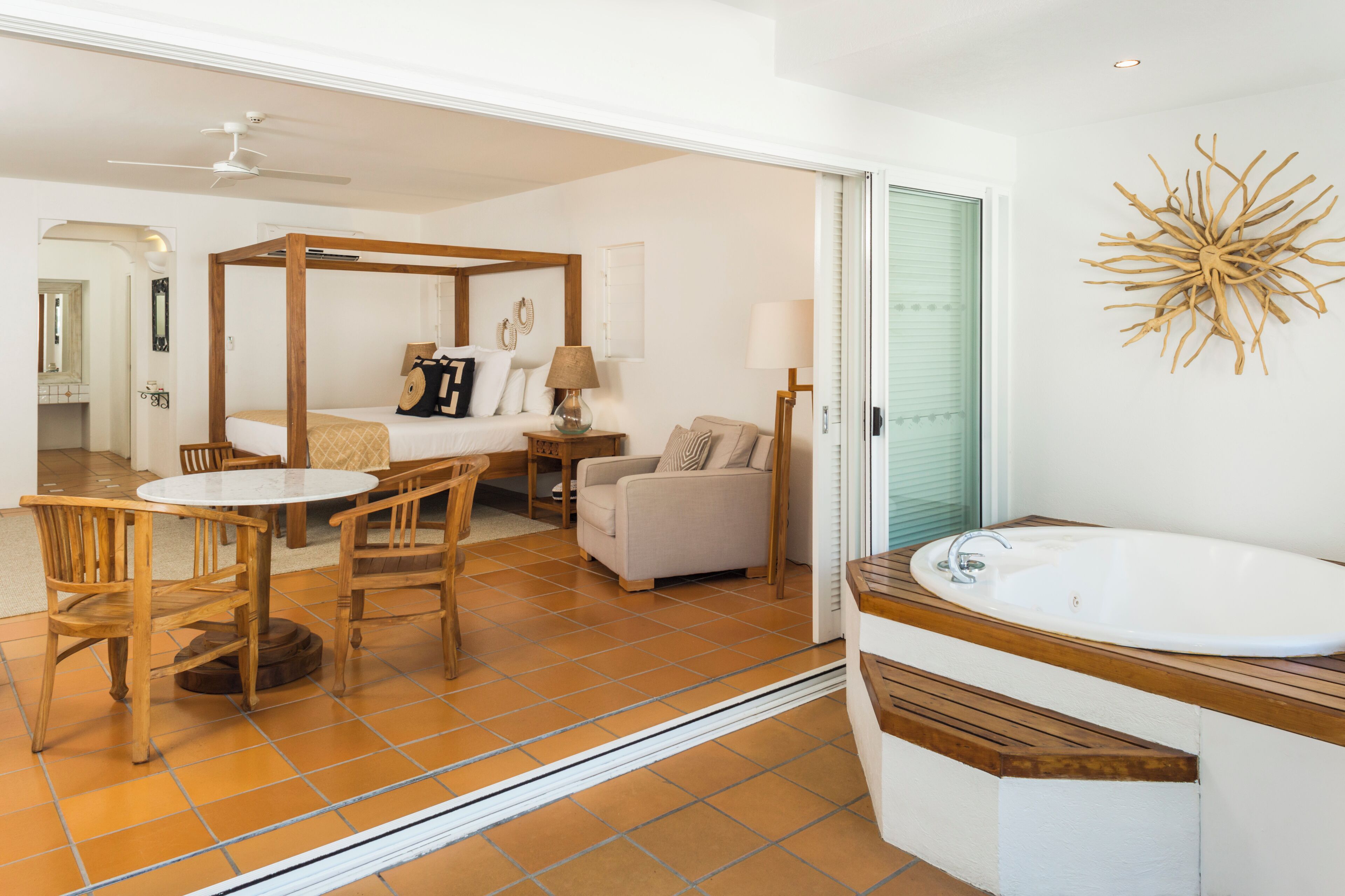A bedroom with a four-poster bed, a sitting area with a table and chairs, a sofa, and a bathroom with a bathtub and sink.