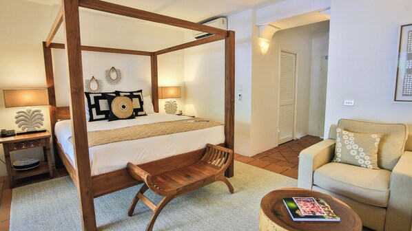 Una cama con dosel de madera, una mesita de noche con lámpara, una silla, un sofá y una pequeña mesa redonda con un libro.