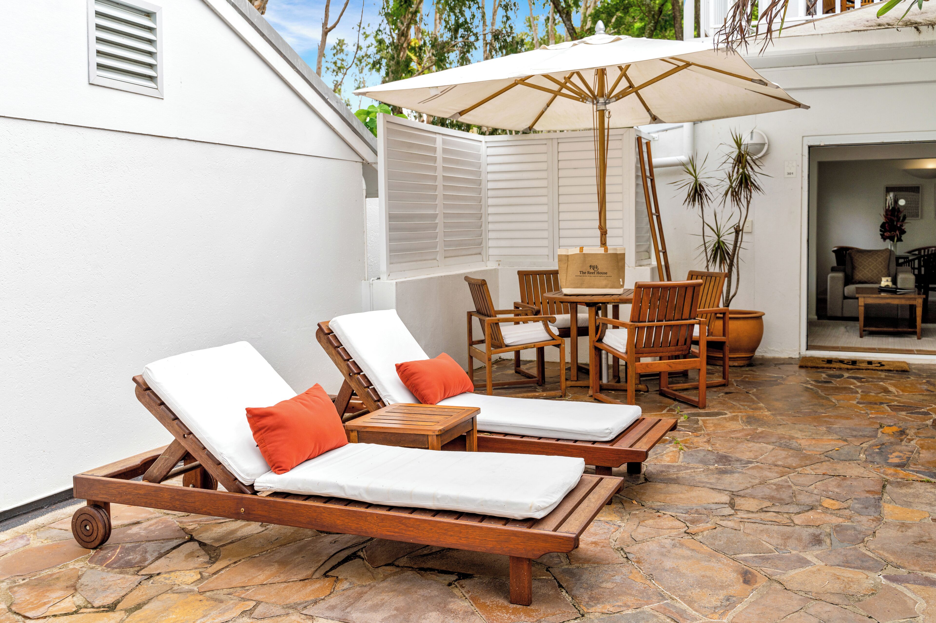 Een terras met twee houten loungestoelen, een tafel en een parasol.