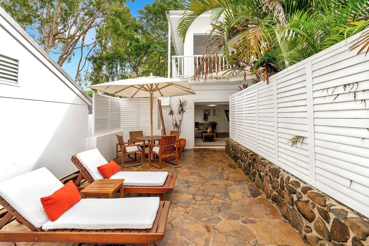 A patio with lounge chairs, a table, and an umbrella.