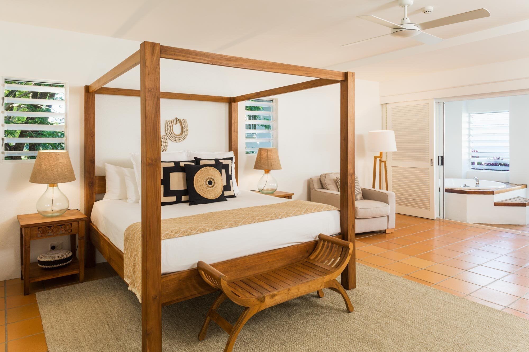 A four-poster bed with a wooden bench, a bedside table, and a lamp.