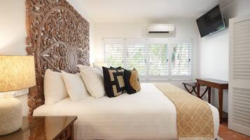 A bedroom with a large bed, a wooden headboard, a TV, an air conditioner, and a window with blinds.