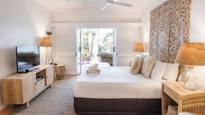 Ein Schlafzimmer mit einem Bett, einem Fernseher, zwei Lampen, einem Deckenventilator und Blick durch eine Schiebetür.