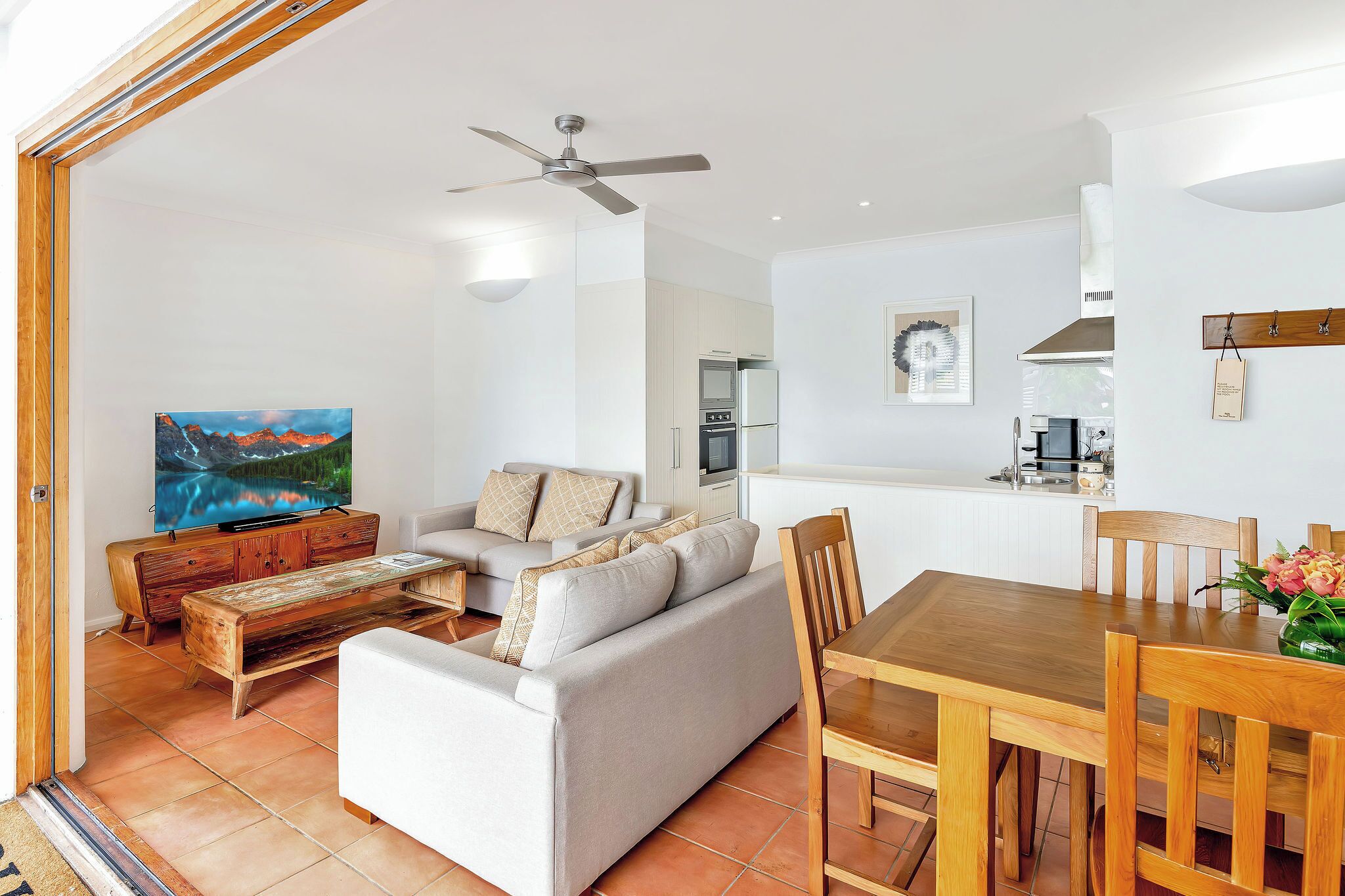 Un salon moderne avec un canapé, une table basse et une table à manger. On peut y voir un téléviseur, un ventilateur de plafond et un coin cuisine.