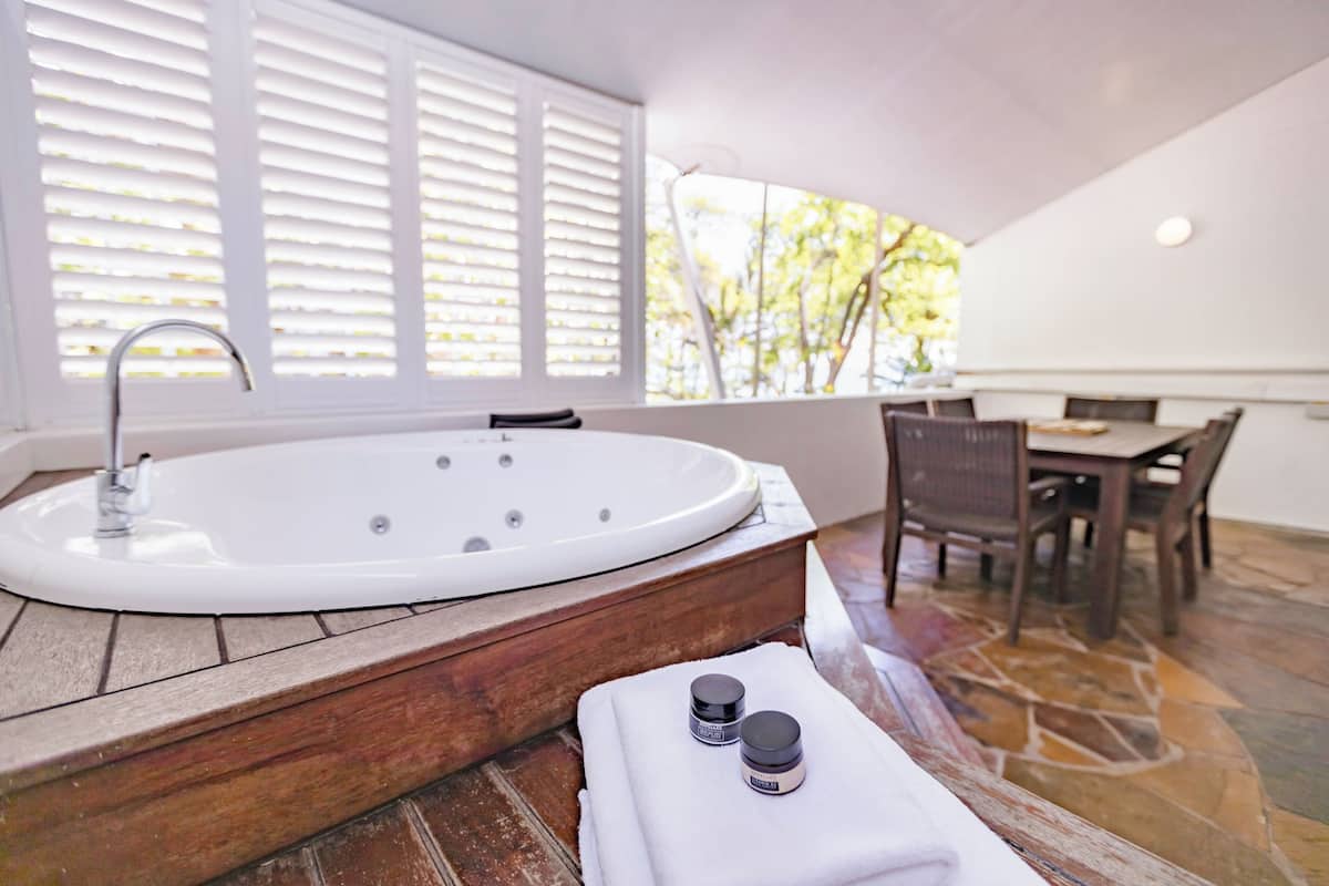 A modern bathroom with a freestanding bathtub, a wooden vanity, and a window with blinds.