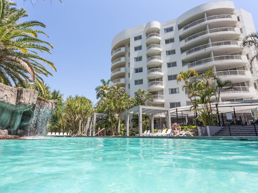 Un hotel con piscina, palmeras y una cascada.