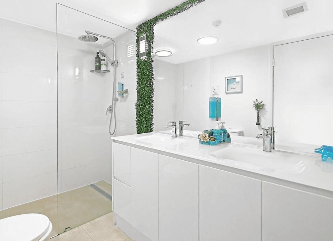Een moderne badkamer met een douchecabine van glas, een wit wastafeltje met spiegel, en een groene plant decoratie.