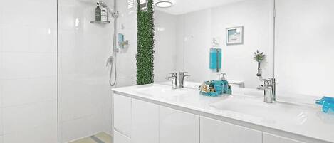 Een moderne badkamer met een douchecabine van glas, een wit wastafeltje met spiegel, en een groene plant decoratie.