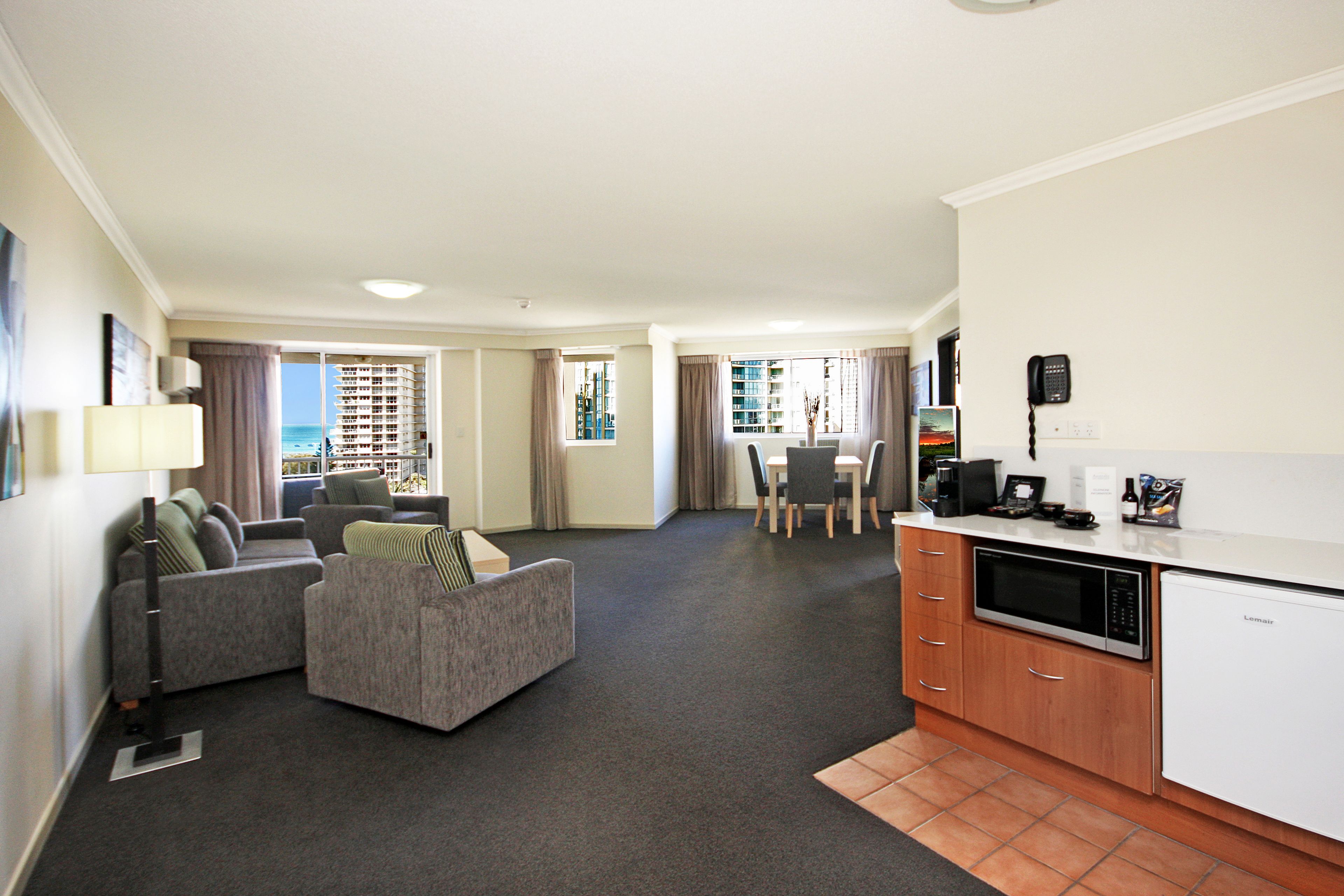 A modern hotel room with a living area, kitchenette, and a view of the ocean.