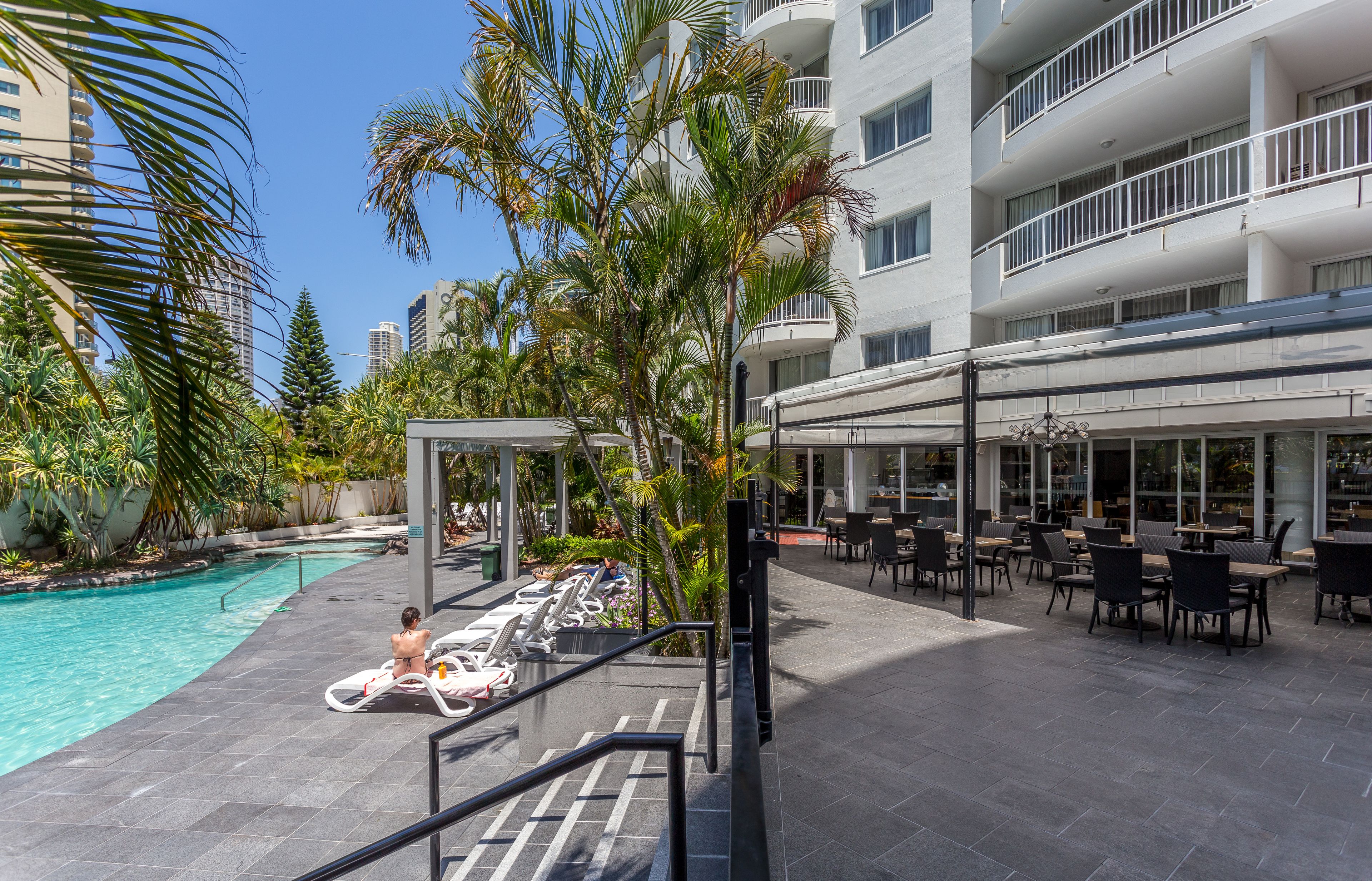 A hotel pool area with lounge chairs, a covered seating area, and a view of the surrounding buildings.