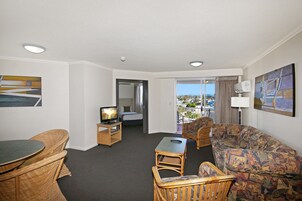 Habitación de hotel con balcón, televisor, sofá, mesa de comedor y muebles de mimbre.
