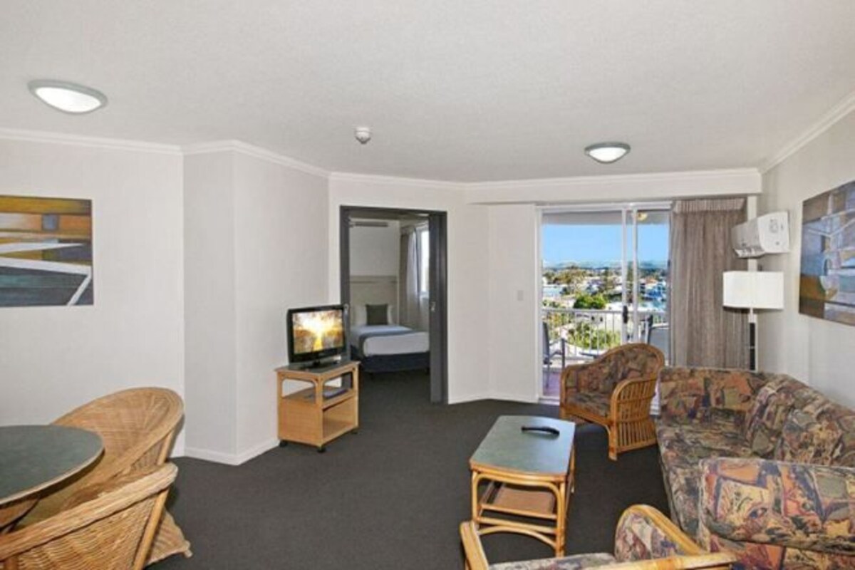 Een hotelkamer met balkon, televisie, bank, eettafel en stoel.