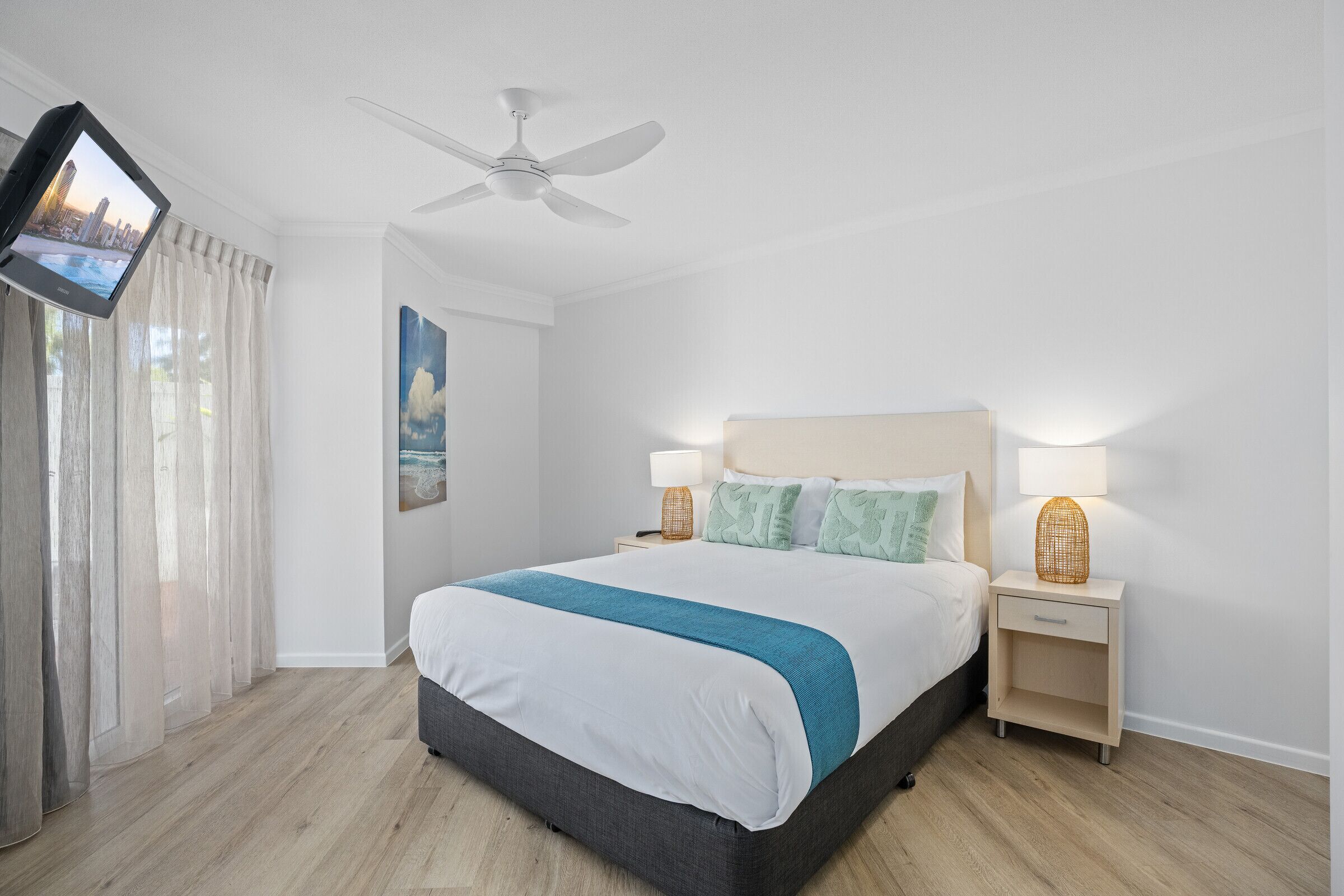 A modern hotel room with a bed, bedside tables, a ceiling fan, and a TV mounted on the wall.