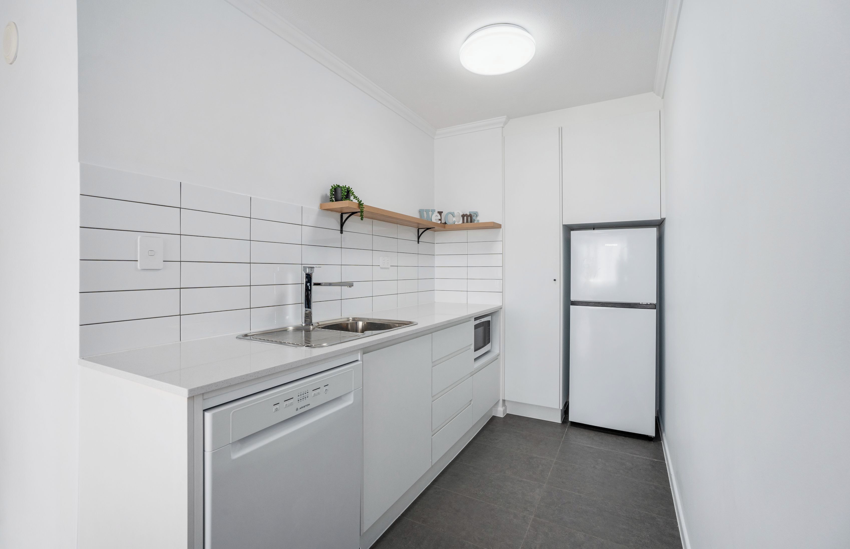 A modern kitchen with white cabinetry, a stainless steel sink, a built-in oven, and a double-door refrigerator.