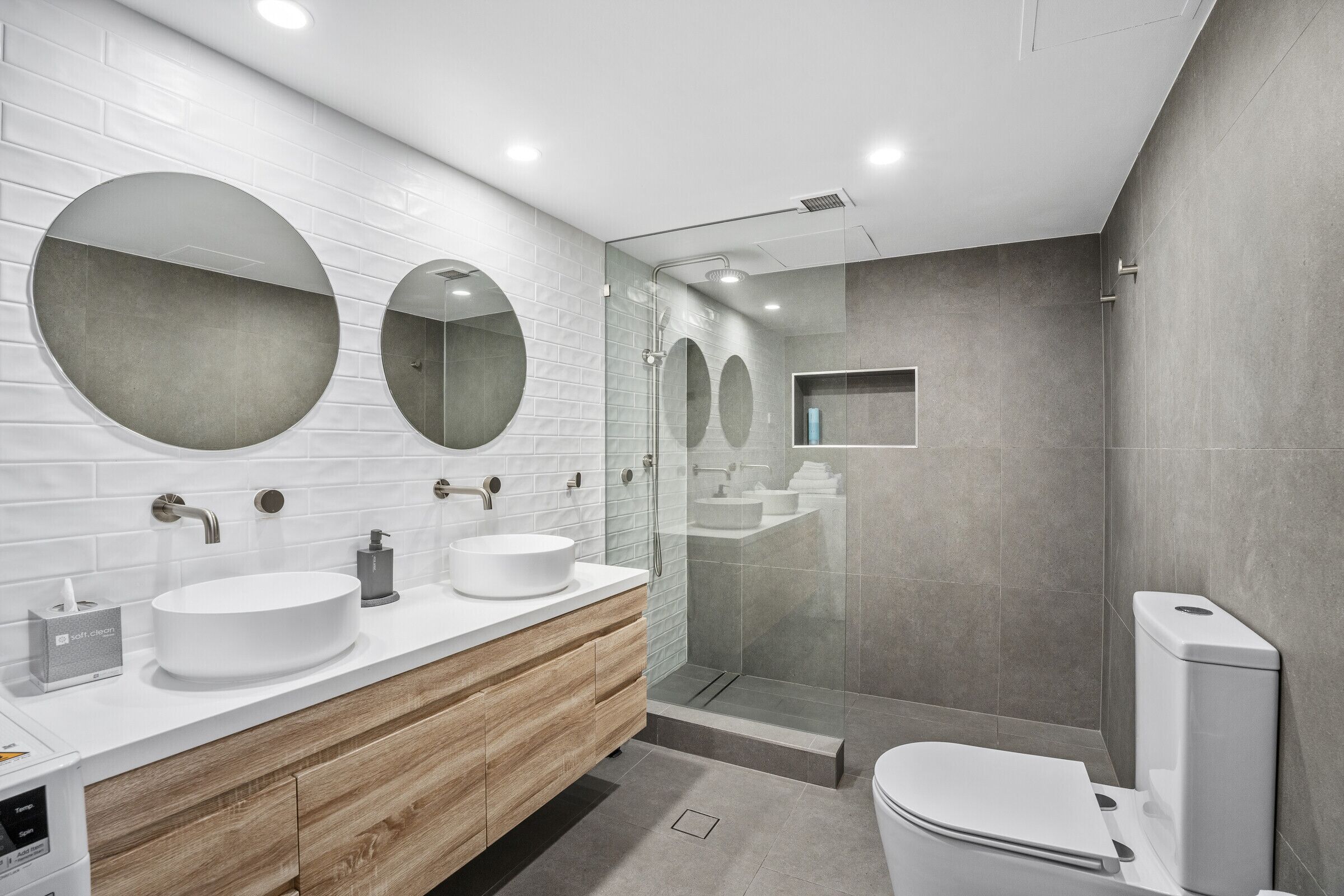 A modern bathroom with two sinks, a toilet, and a glass-enclosed shower.