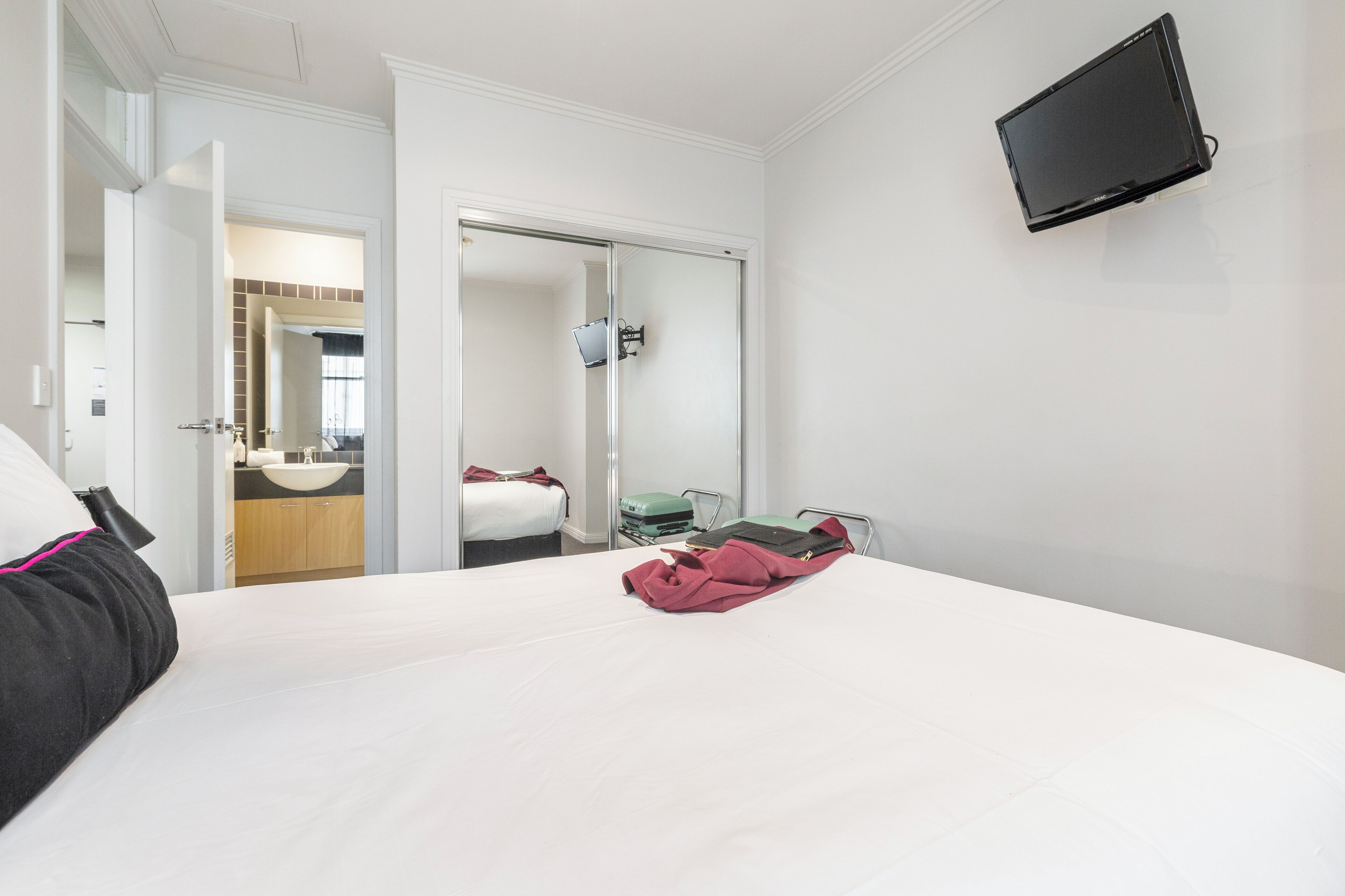 Une chambre d’hôtel avec un lit, un téléviseur fixé au mur et une salle de bain visible à travers une porte ouverte.