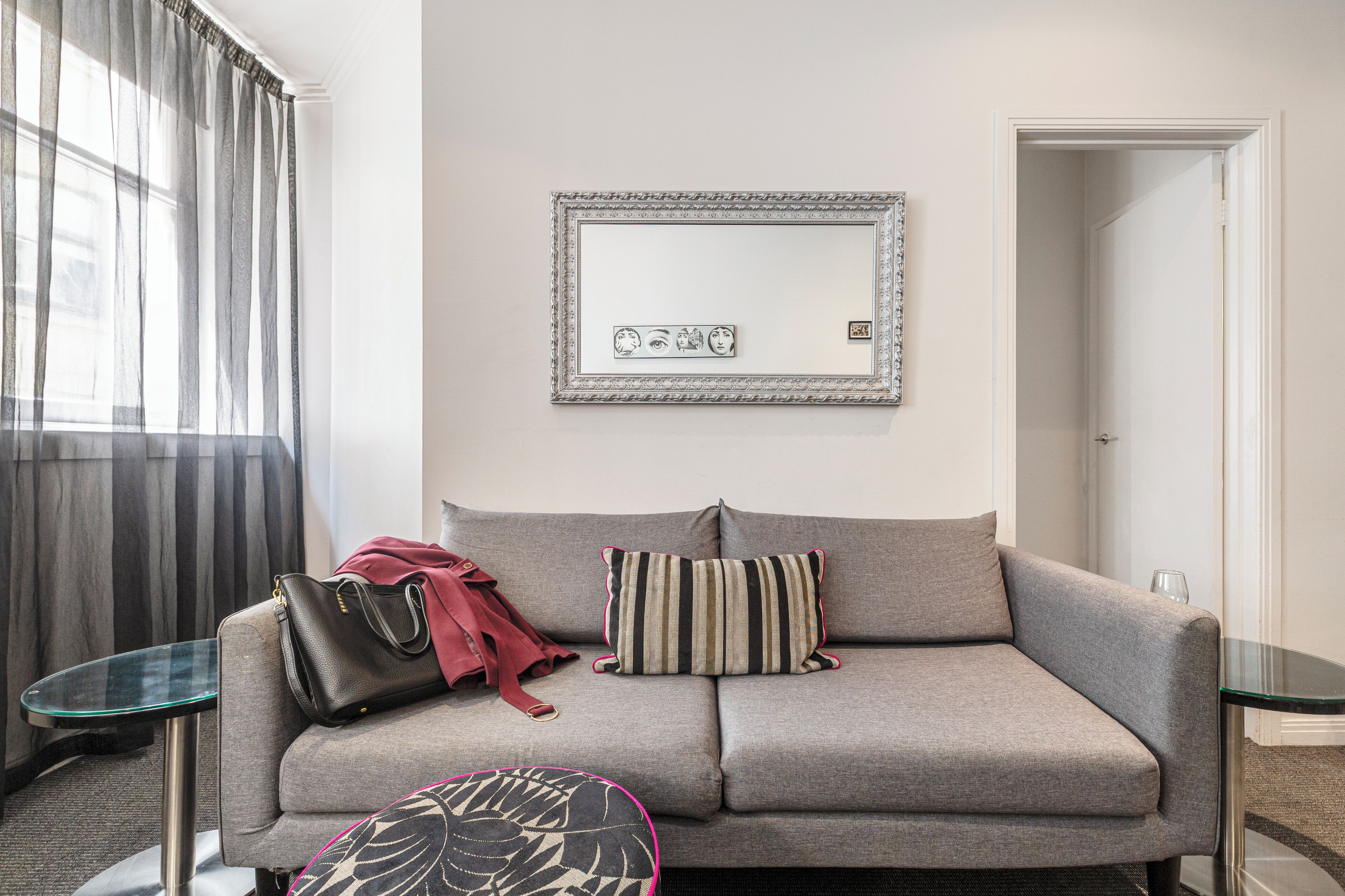A modern living room with a grey sofa, striped pillows, a glass coffee table, and a black handbag on the sofa.