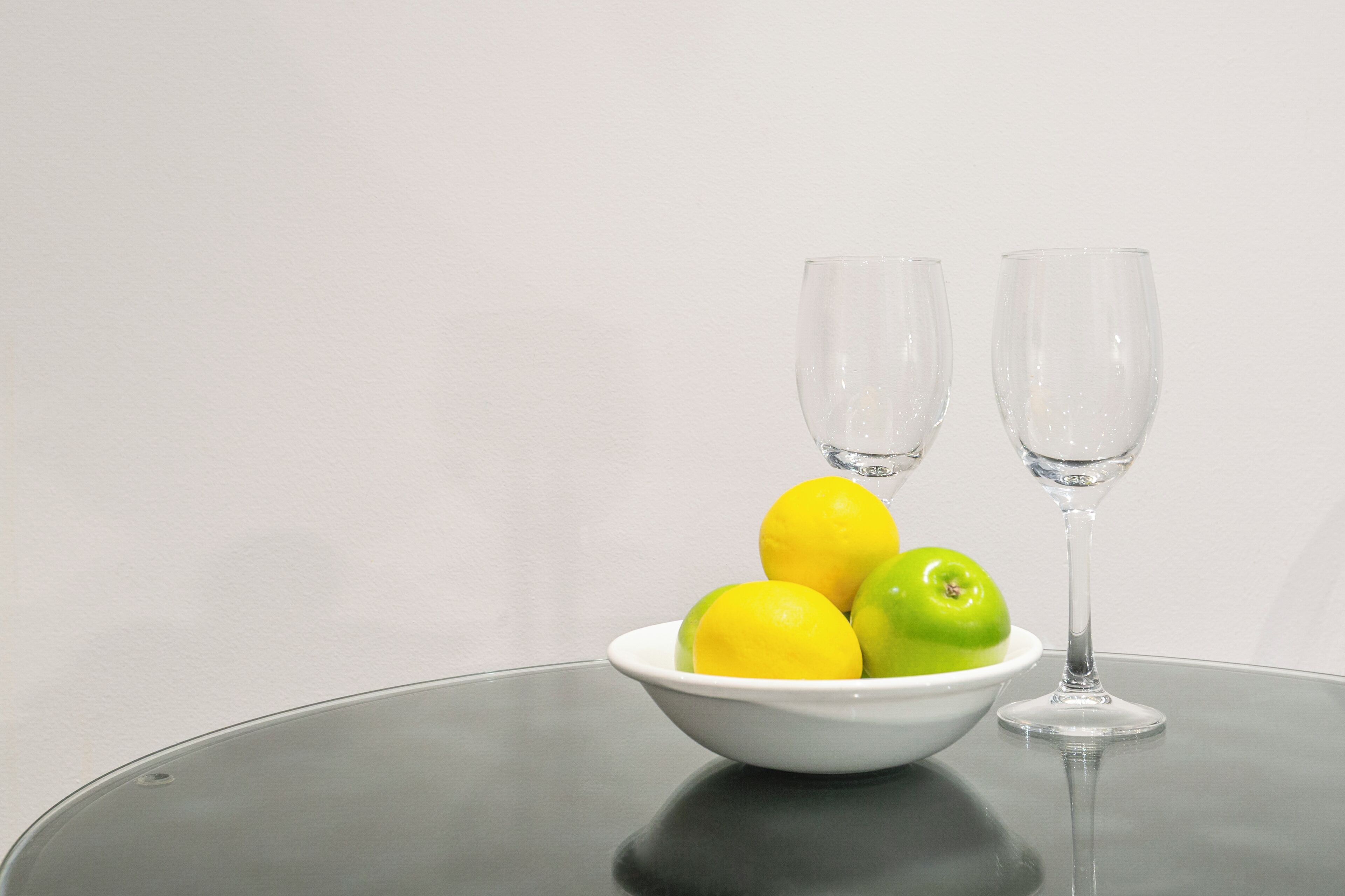 Een schaal fruit op een tafel, met twee lege wijnglazen.