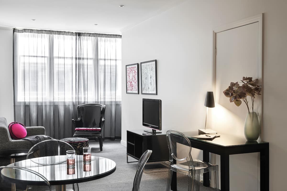 Un salon moderne avec une table ronde en verre, un meuble TV noir et un canapé agrémenté d'un coussin rose.