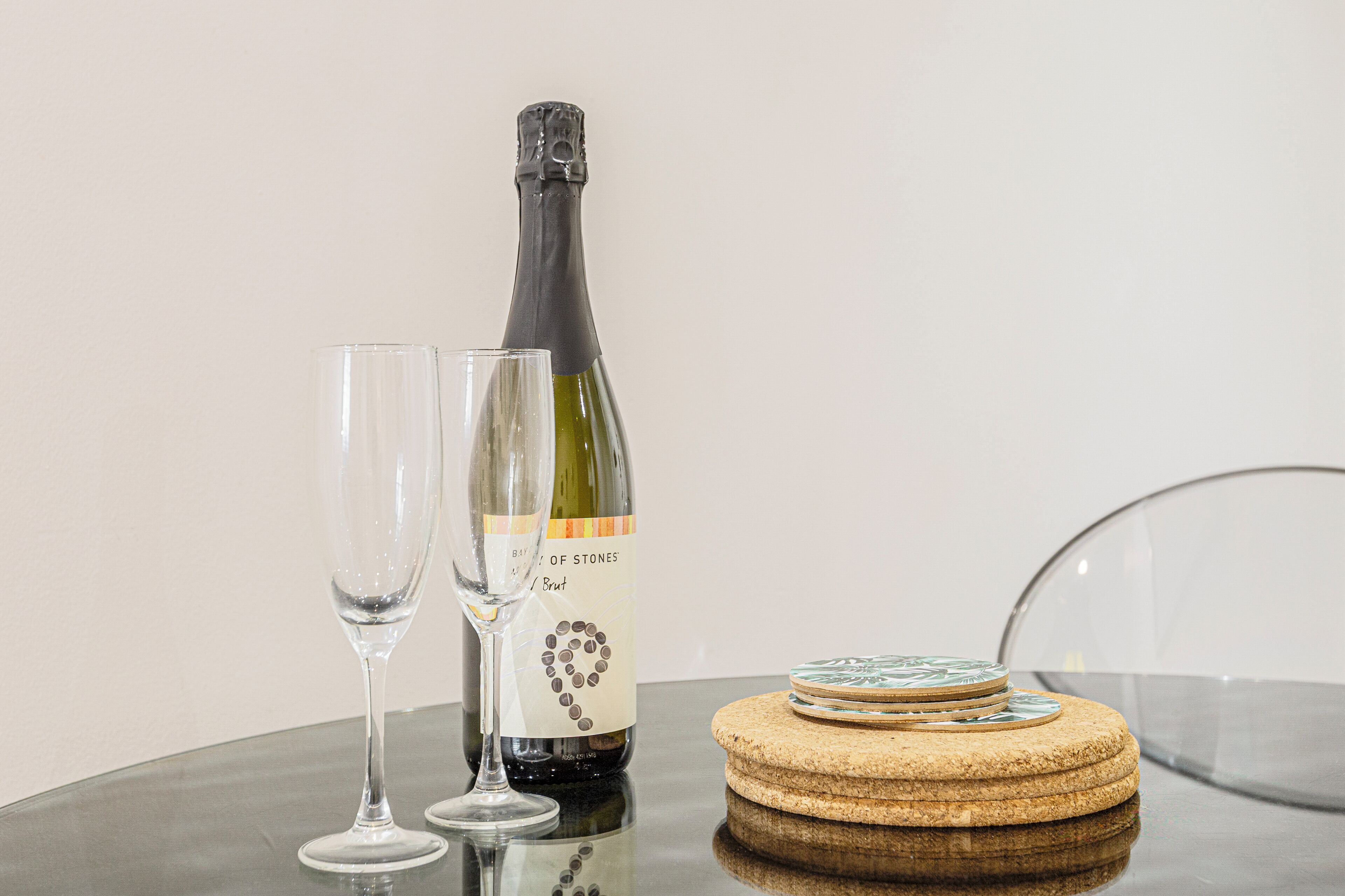 Uma garrafa de vinho, dois copos e suportes para copos em uma superfície refletora.