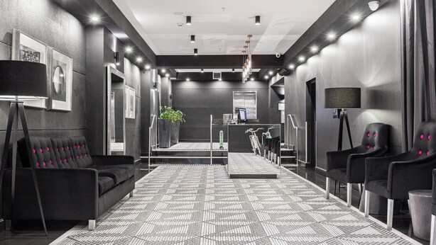 Um lobby de hotel moderno com piso em padrão preto e branco, balcão de recepção e assentos em couro preto.