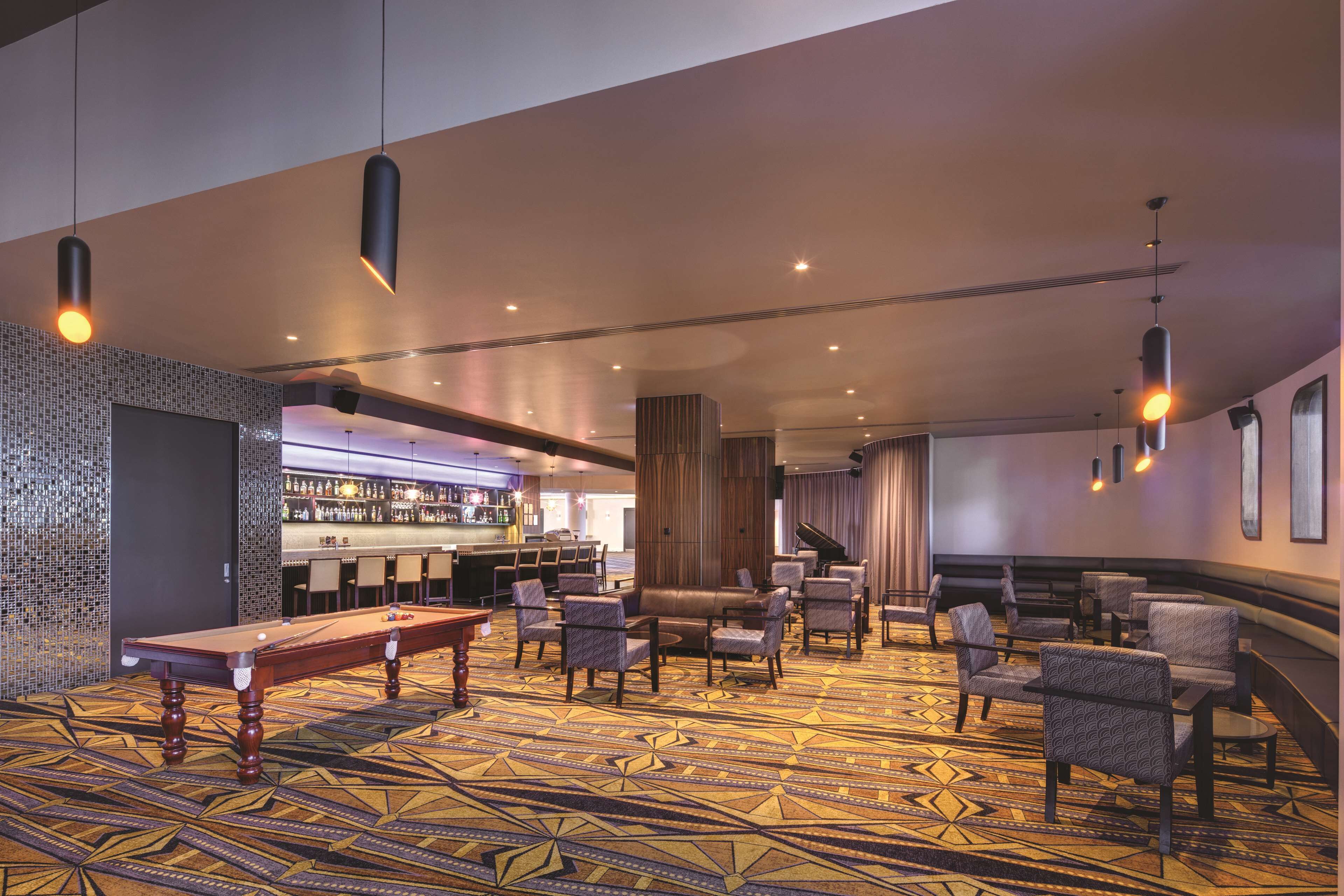 A hotel lobby with a pool table, seating area, bar, and a patterned carpet.