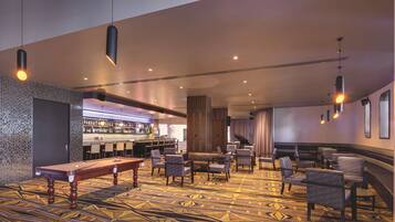 A hotel lobby with a pool table, seating area, bar, and a patterned carpet.