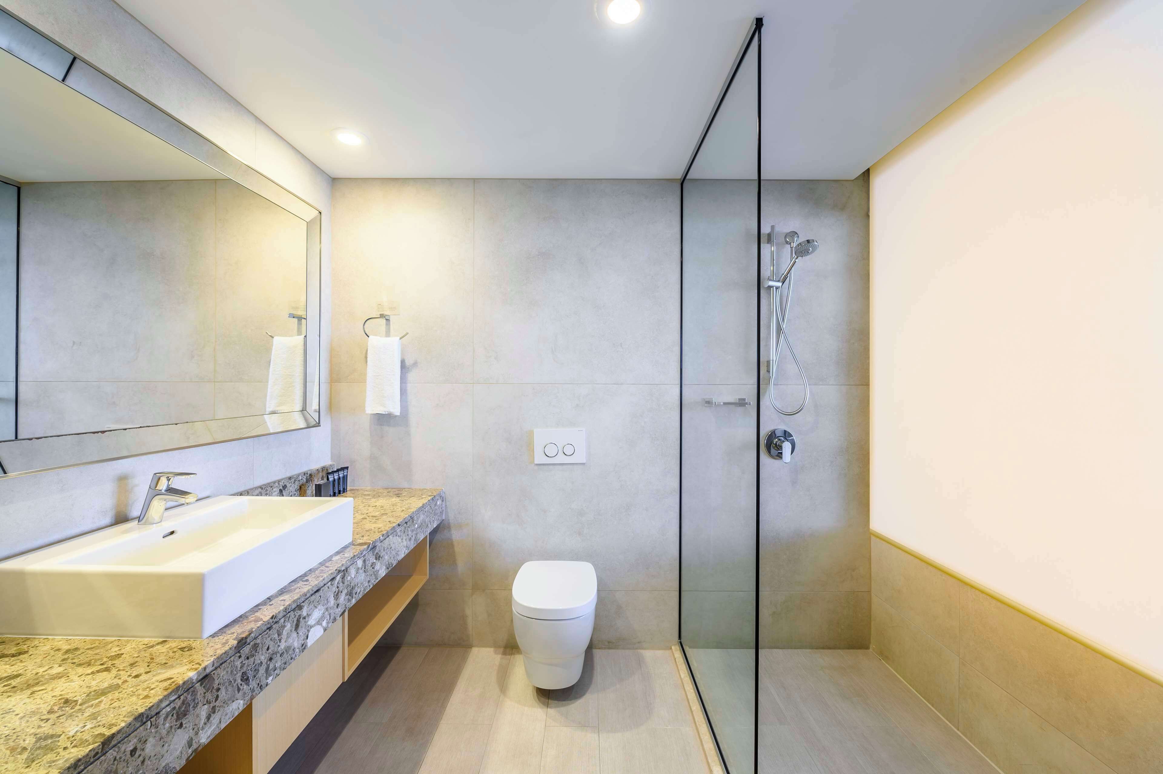 A modern bathroom with a large mirror, a sink, a toilet, and a glass-enclosed shower.