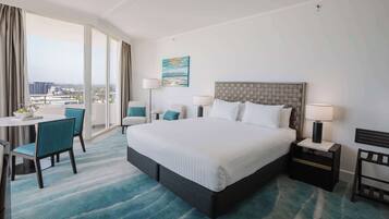 Habitación de hotel con una cama grande, un escritorio con silla, vista a la ciudad desde un balcón y un cuadro en la pared.