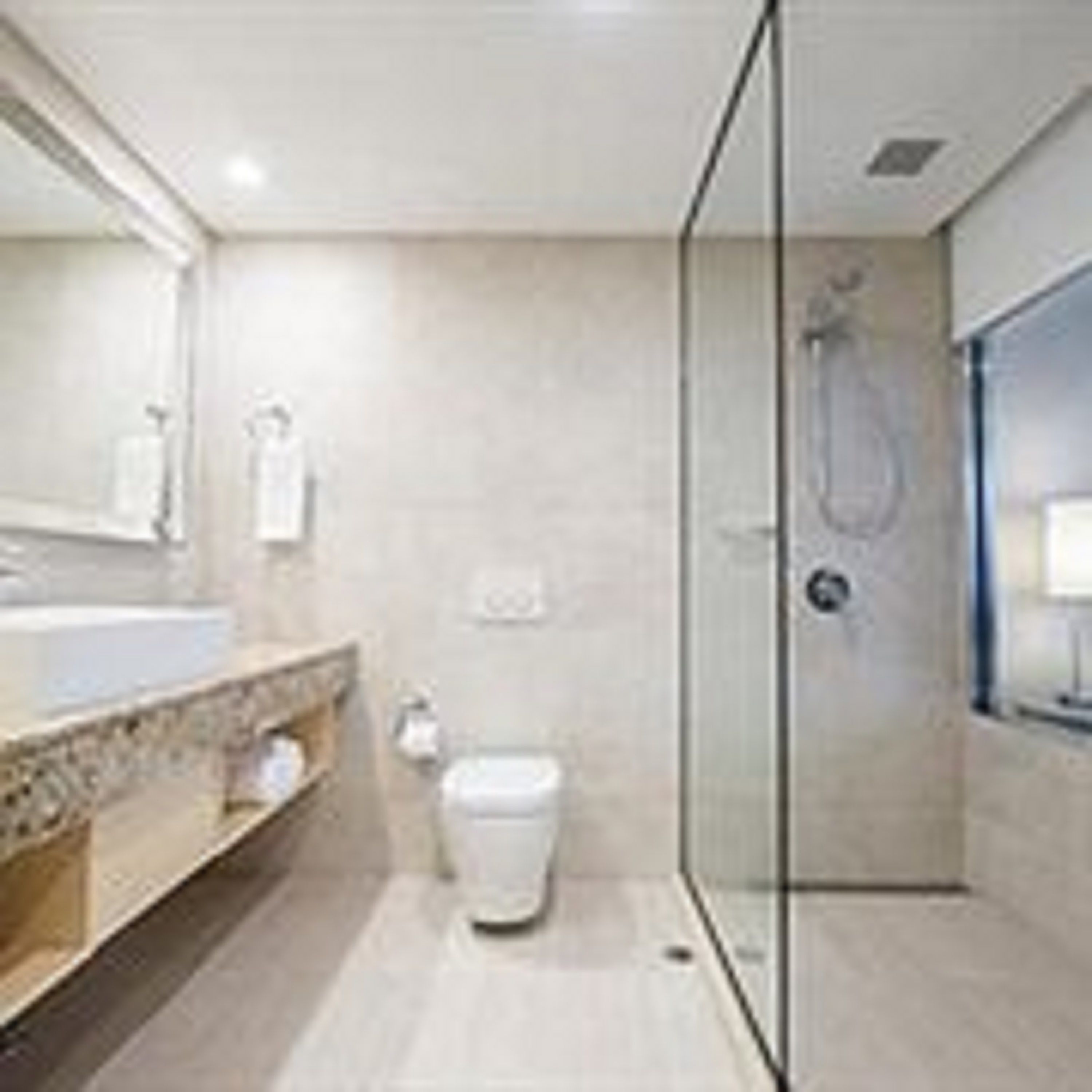 A modern bathroom with a glass shower enclosure, a large mirror, and a wooden vanity.