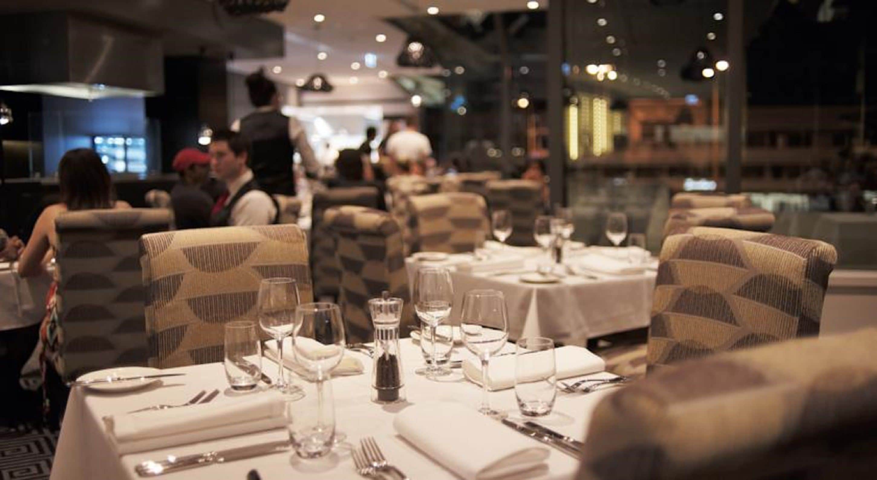 A restaurant interior with tables set for dining, chairs, and a view of the cityscape.