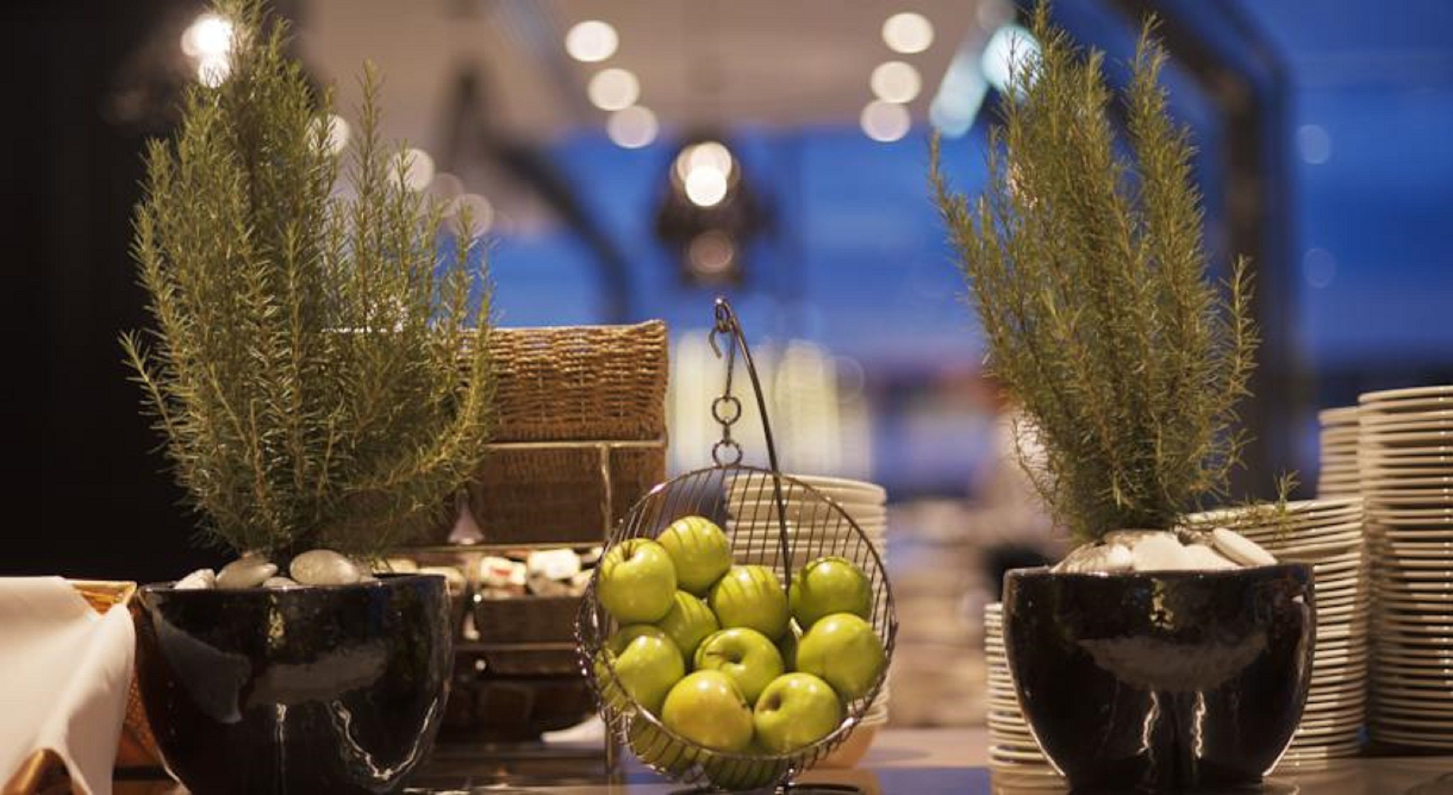 A table with potted plants, a bowl of green apples, and stacked plates.