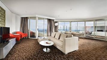 A modern hotel room with a large sofa, a coffee table, and a view of the city.