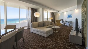 A modern hotel room with a large window offering a view of the ocean, a sofa, a small round table, and a desk with a computer. - Rendezvous Hotel Perth Scarborough (Scarborough)