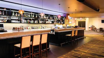 Una zona de bar con varios taburetes, una barra y estantes llenos de botellas.