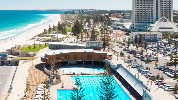 A large swimming pool with a curved deck, surrounded by a parking area and a beach. - Rendezvous Hotel Perth Scarborough (Scarborough)
