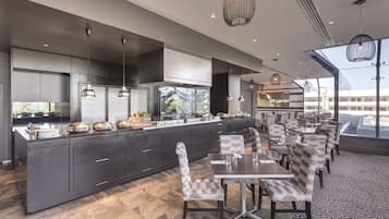 Cozinha moderna com uma ilha grande, armários escuros e luminárias pendentes.