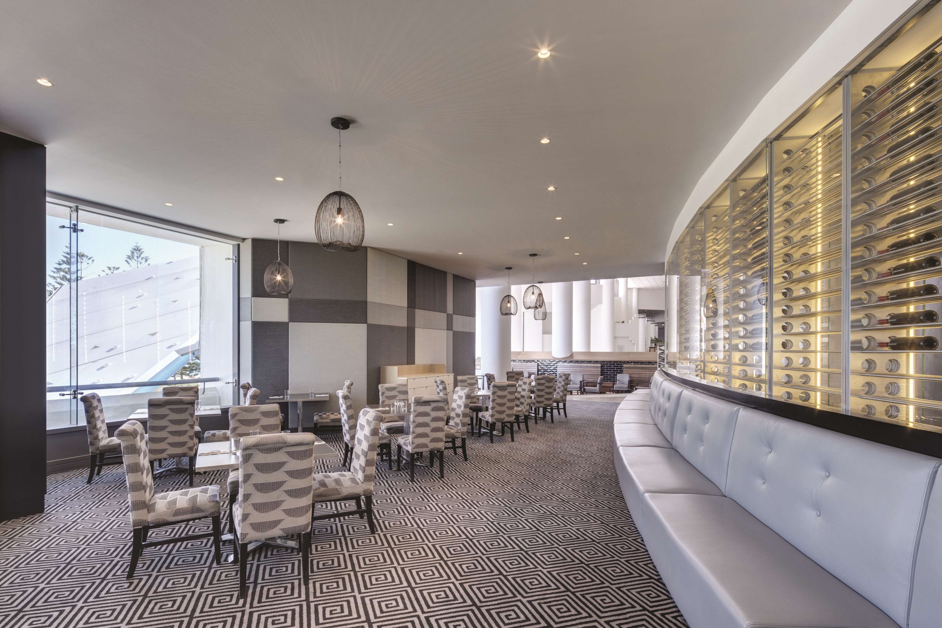 A modern hotel lobby with a checkered floor, seating area, and a wine display wall.