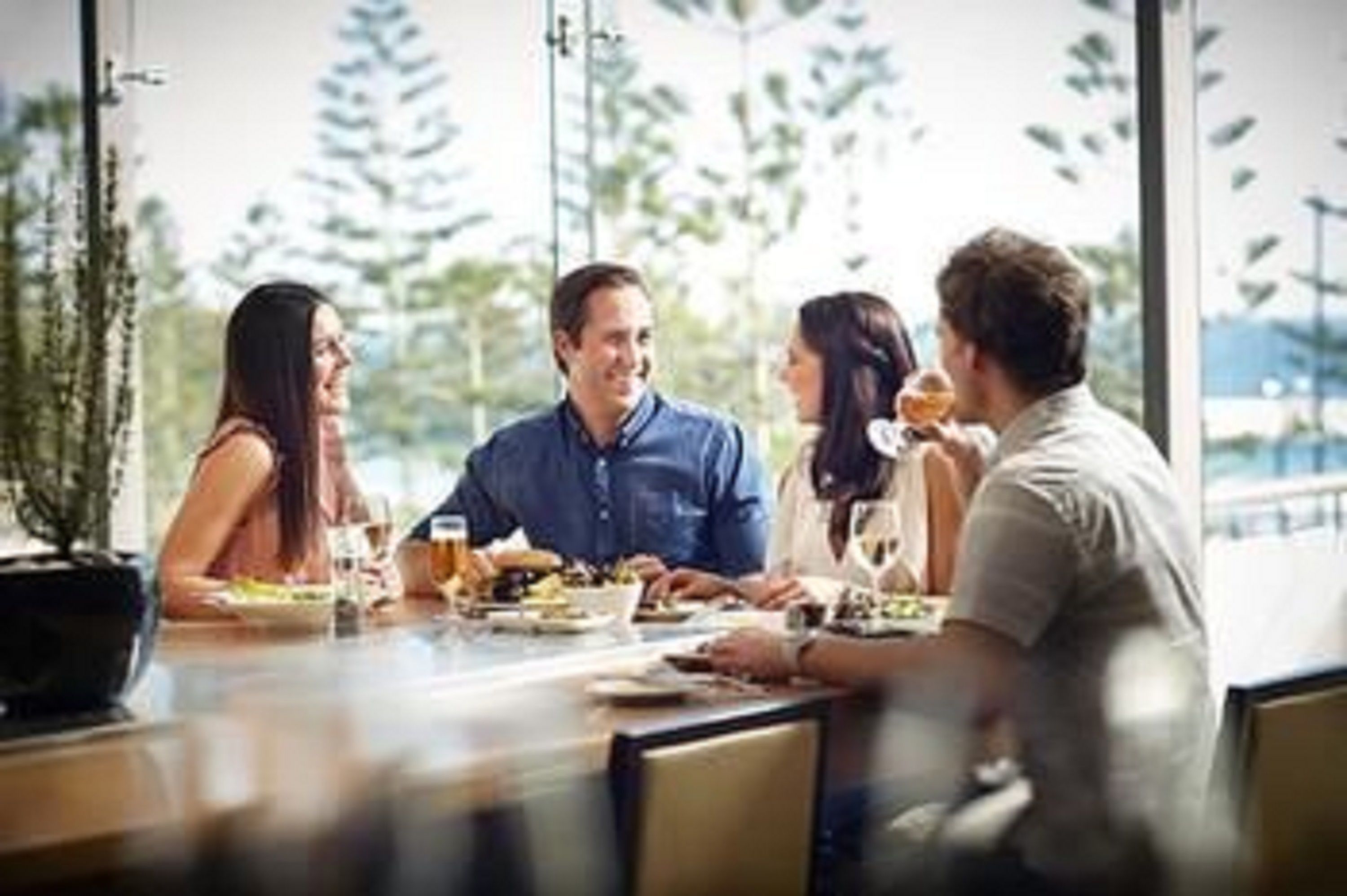 A group of people dining at a table with a view of trees and a body of water.