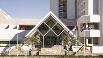 La entrada al Rendevous Grand Hotel, con un diseño arquitectónico moderno, que presenta un llamativo frente de vidrio y una escalera que conduce a la entrada.