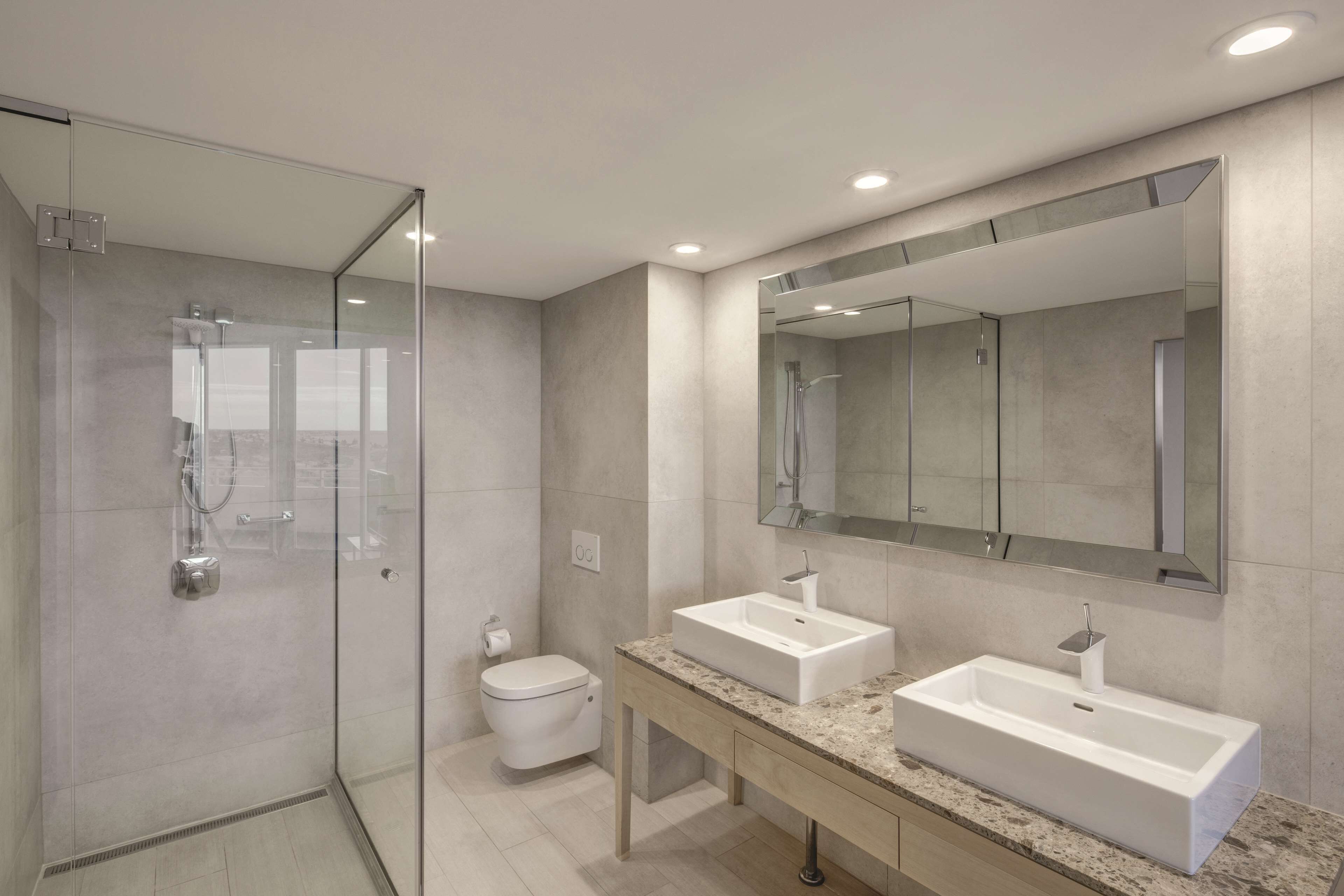 A modern bathroom with a glass-enclosed shower, two sinks, and a large mirror.