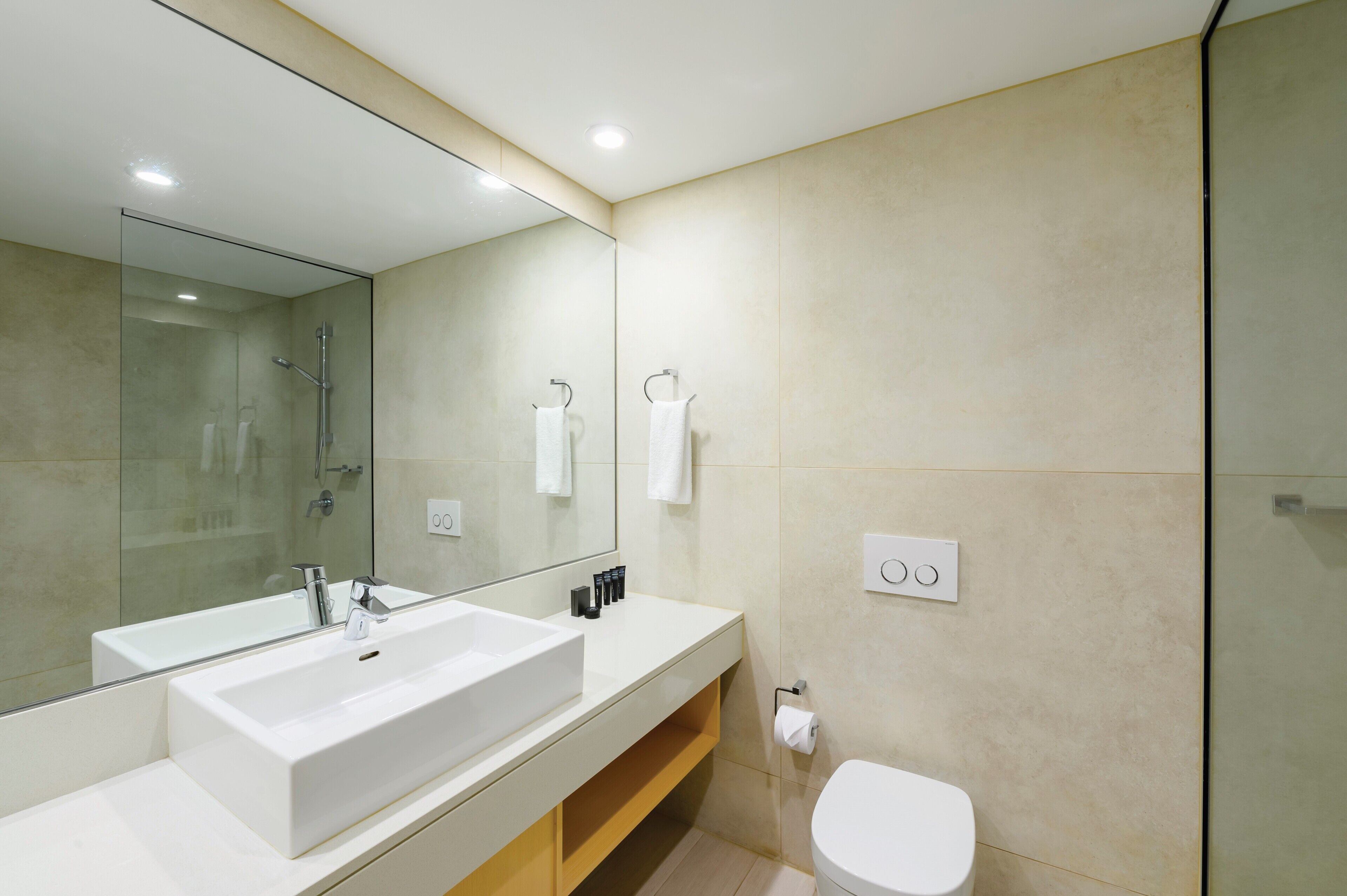 Un baño moderno con un espejo grande, un lavabo blanco, una ducha y un inodoro.