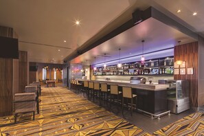 A bar area with a patterned carpet, bar stools, and a well-stocked liquor shelf.