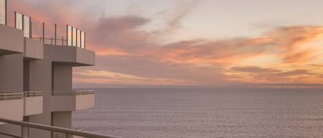 Un bâtiment moderne doté d’un balcon donnant sur une mer calme au coucher du soleil.